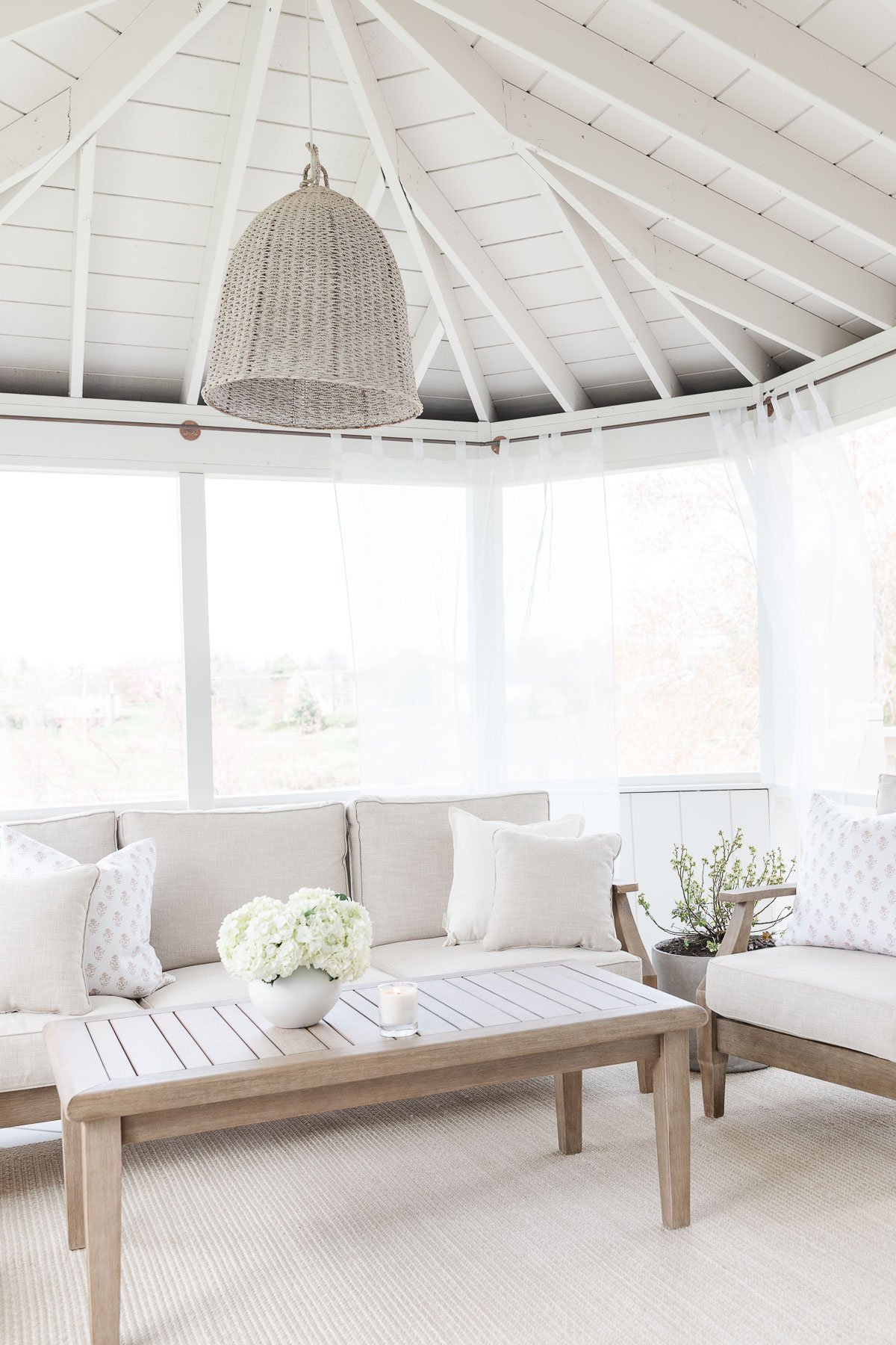 A screened in porch with white furniture and a basket pendant light for added ambiance.