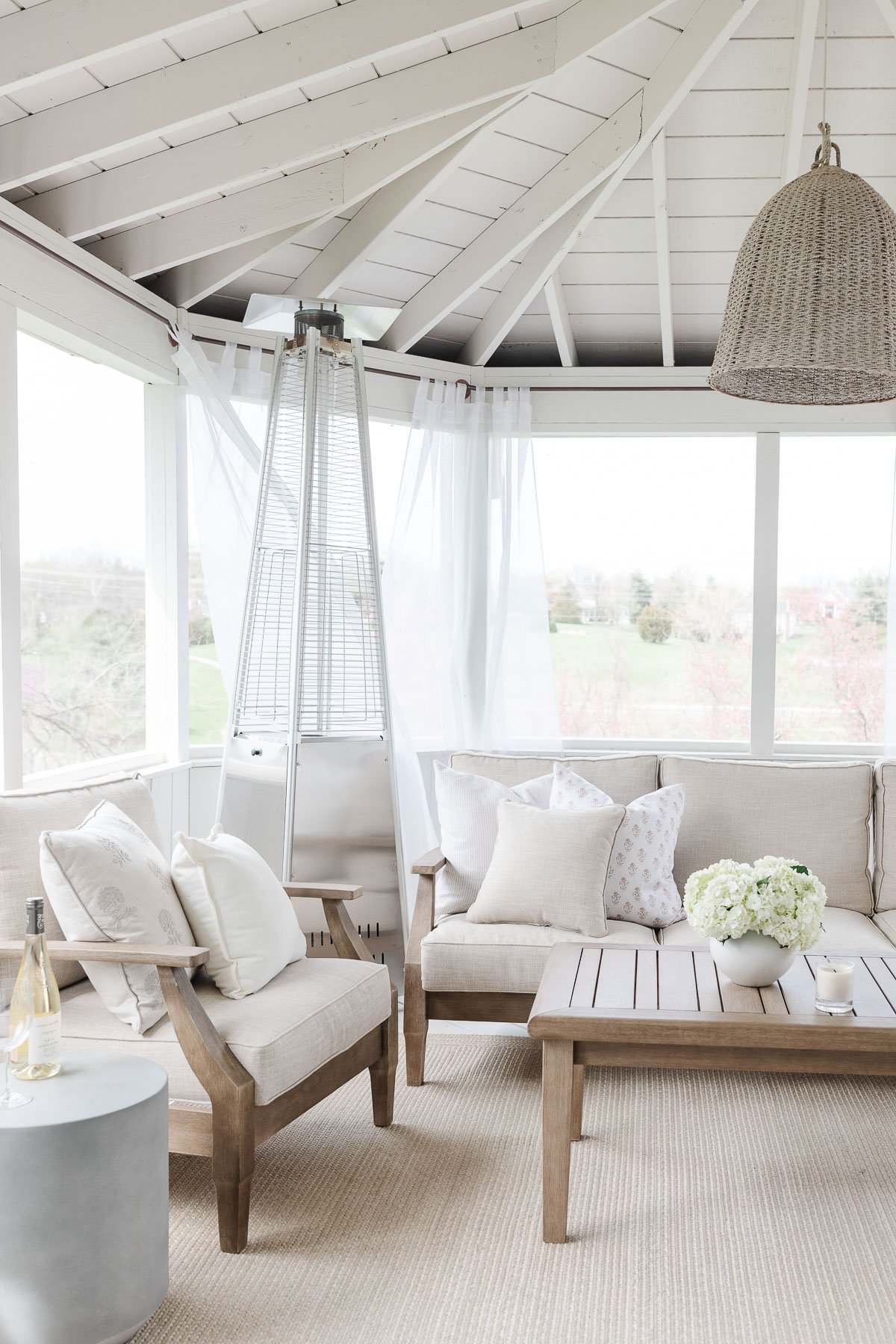 A white screened in porch with a basket pendant light and white furniture.