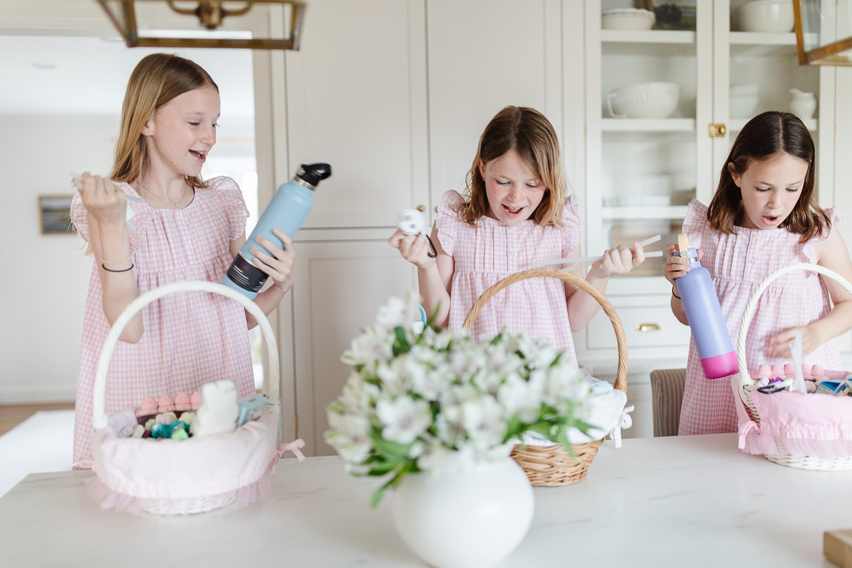 Three little girls are holding easter baskets filled with easter basket fillers in a kitchen.