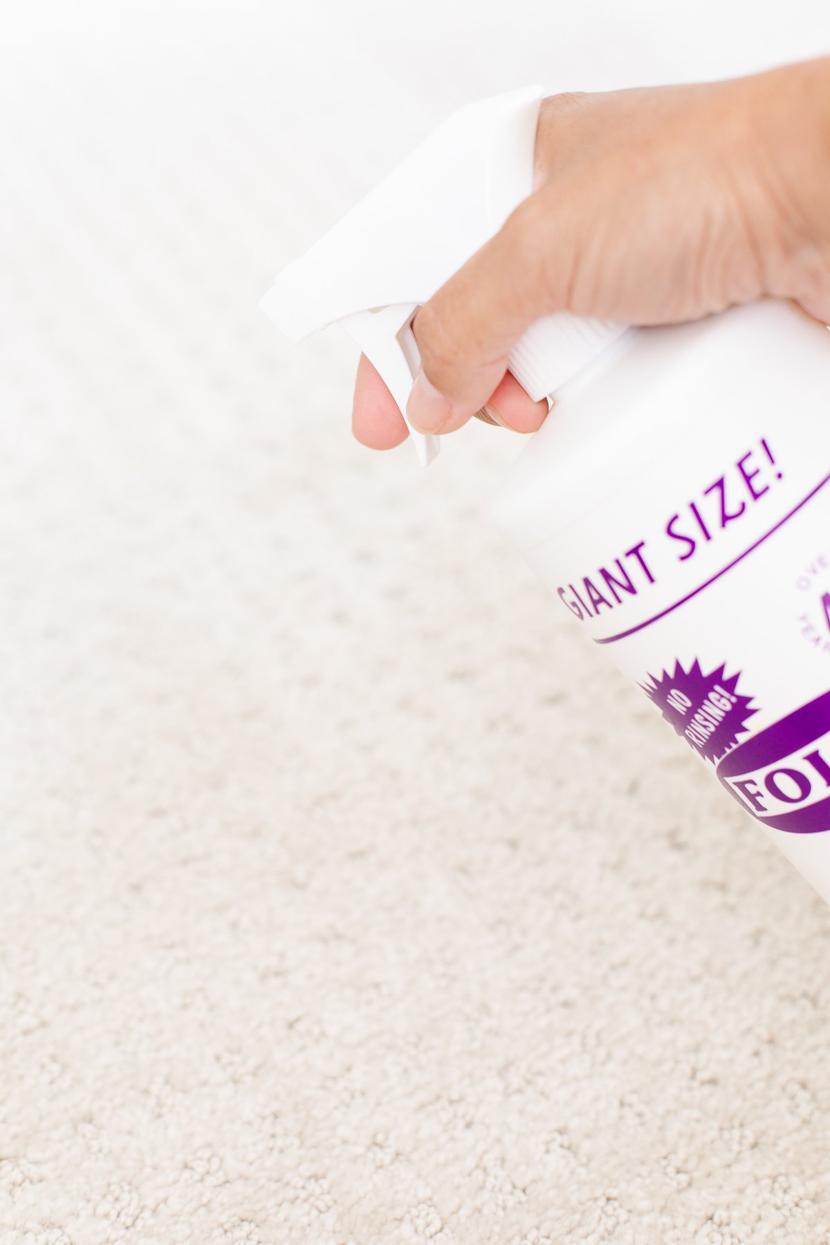 A person is spraying a bottle of Folex carpet cleaner on a carpet.