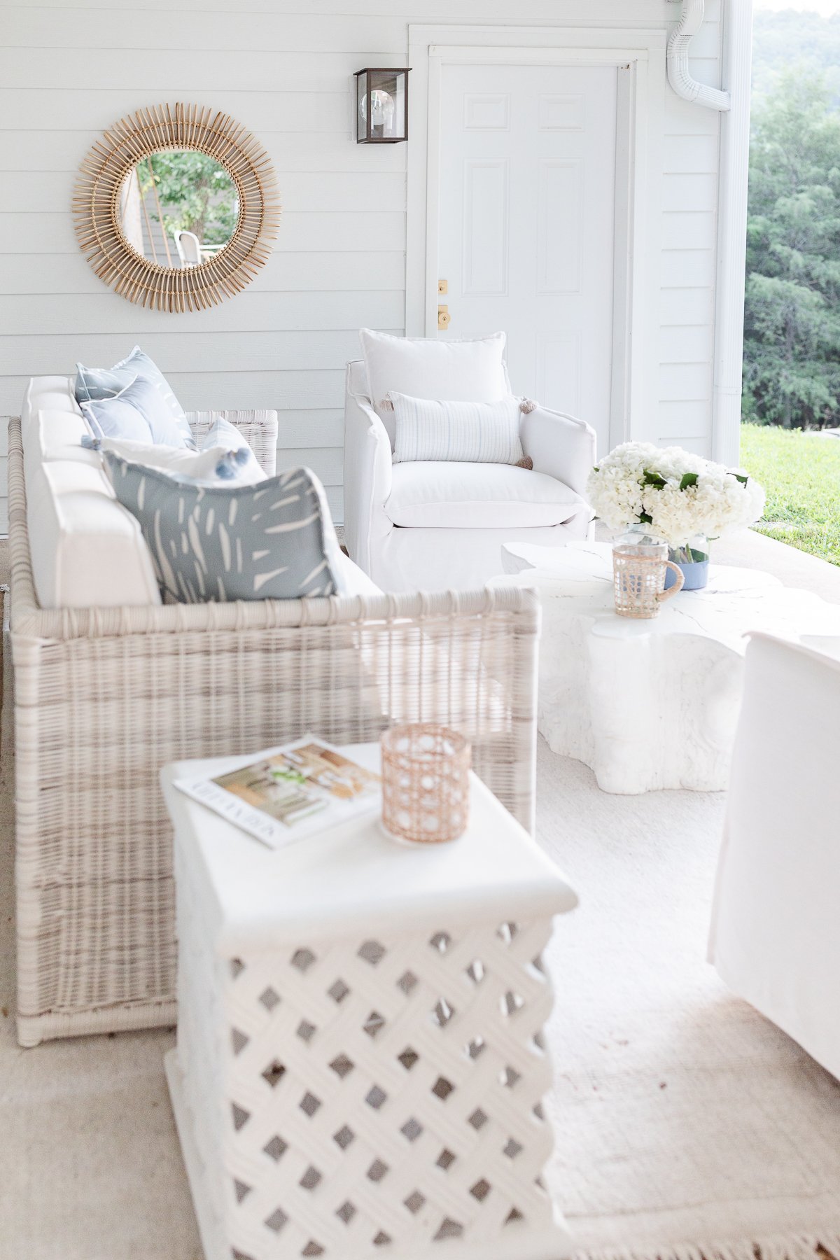 A white living room furnished with wicker furniture and ceramic garden stools.