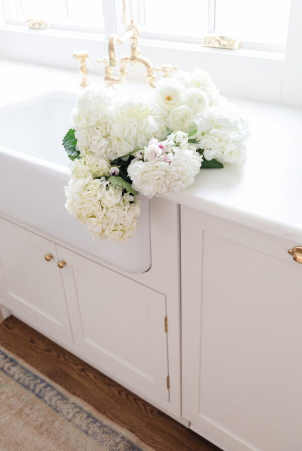 A bunch of white flowers enhancing the minimalist charm of a counter, while creative under sink storage ideas optimize space.