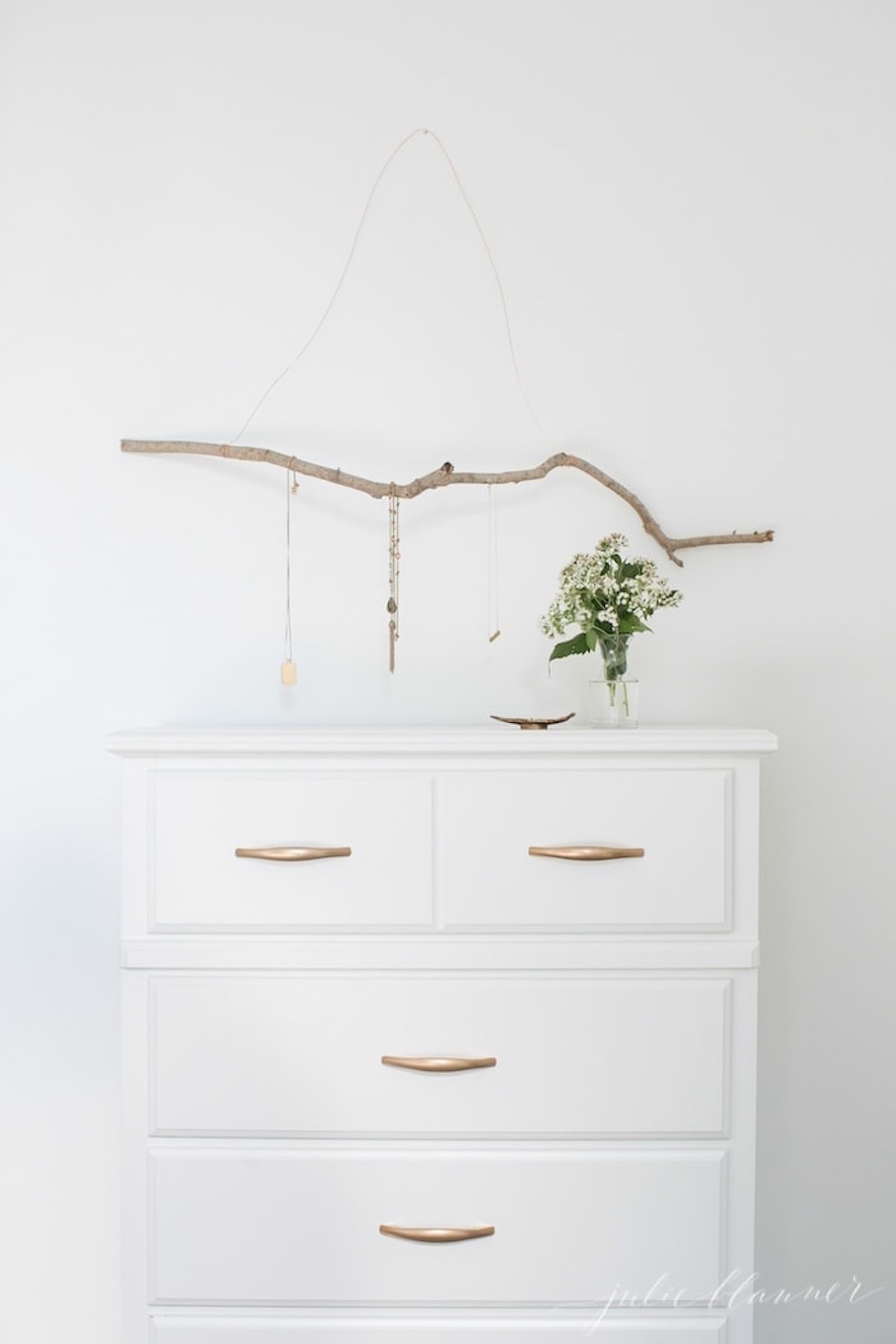 Add a unique touch to your DIY wall decor with this elegant white dresser adorned with a tastefully placed twig.