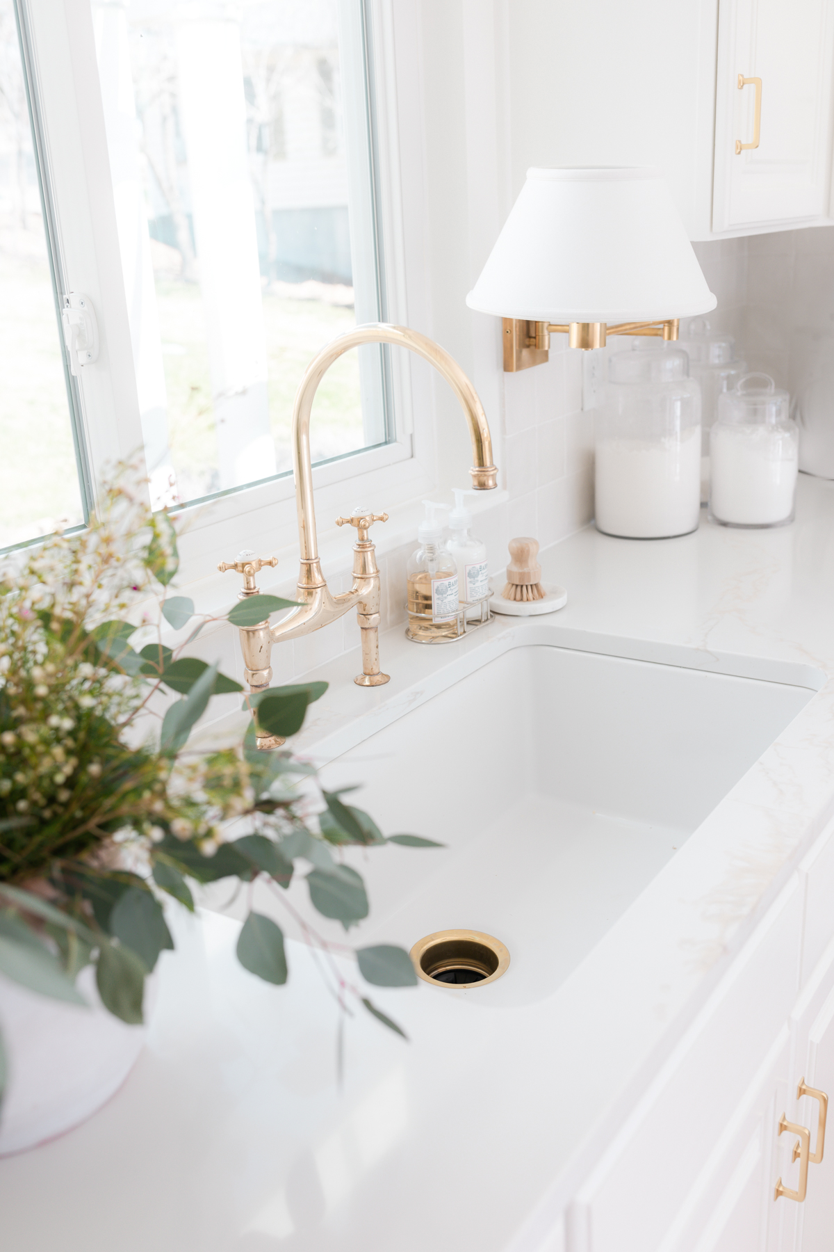 A sink with a gold faucet and a plant in front of a window, showcasing stylish kitchen organization.