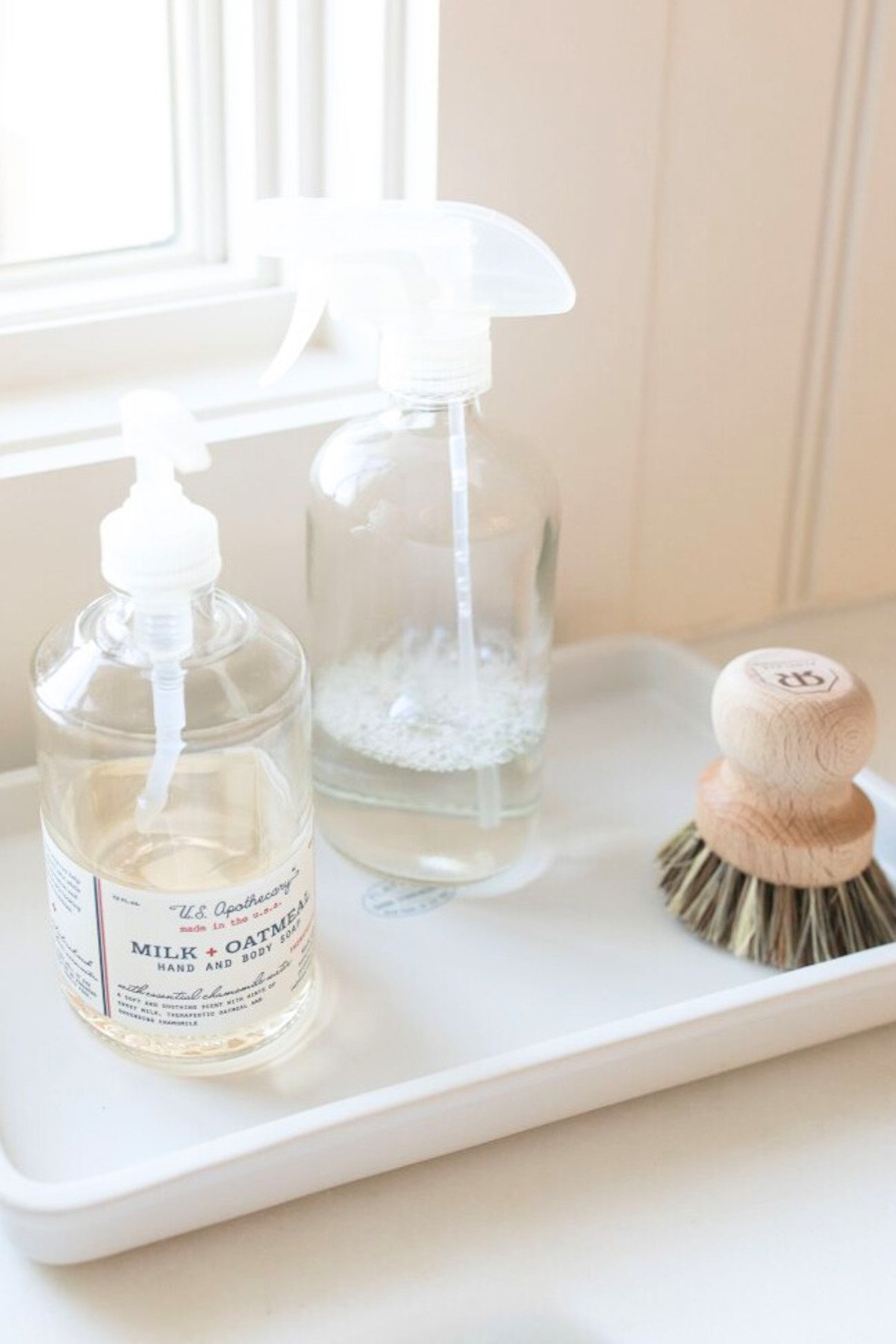 A white tray with bottles of liquid and a brush, perfect for under sink storage