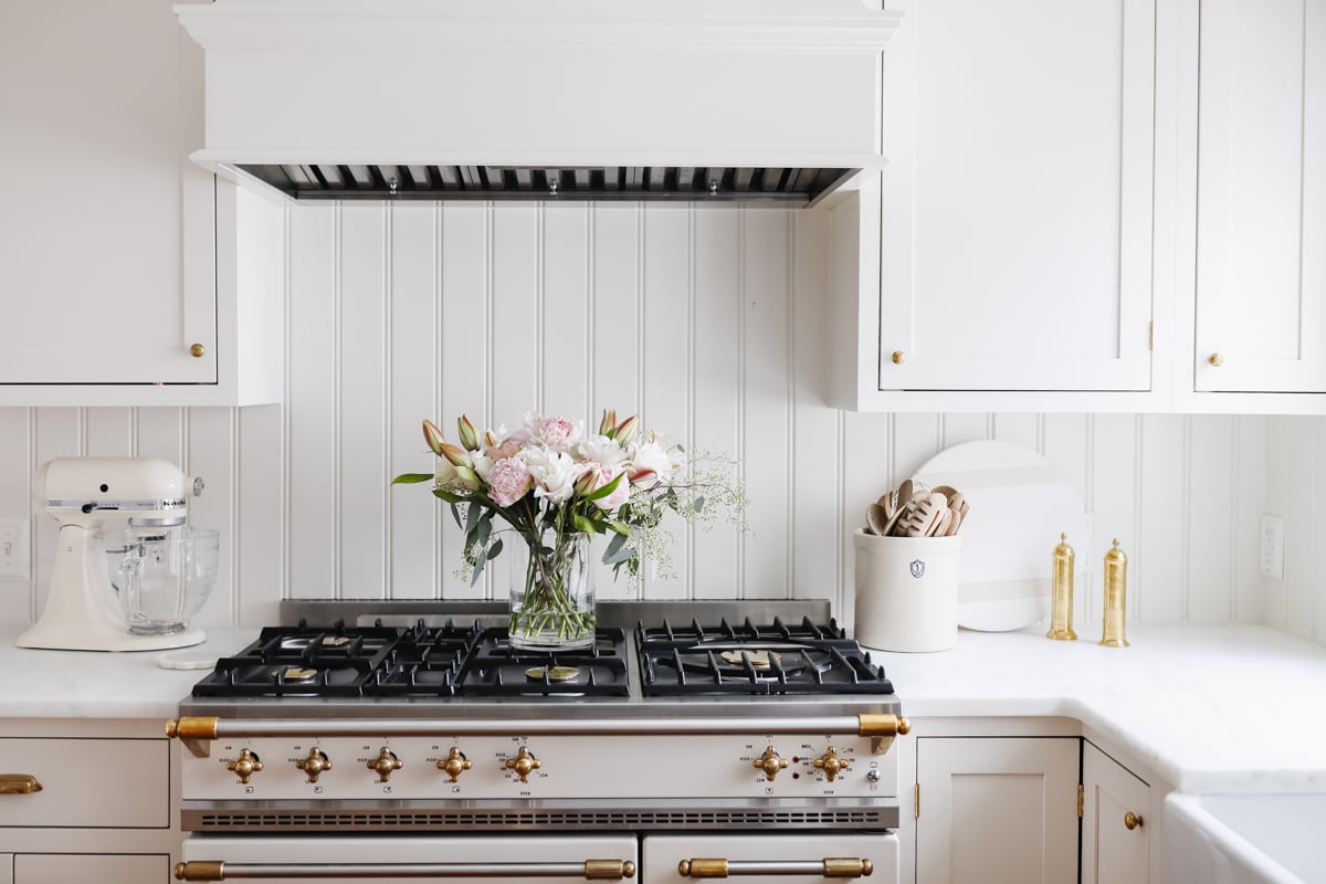 A white kitchen with a lacanche range and flowers.