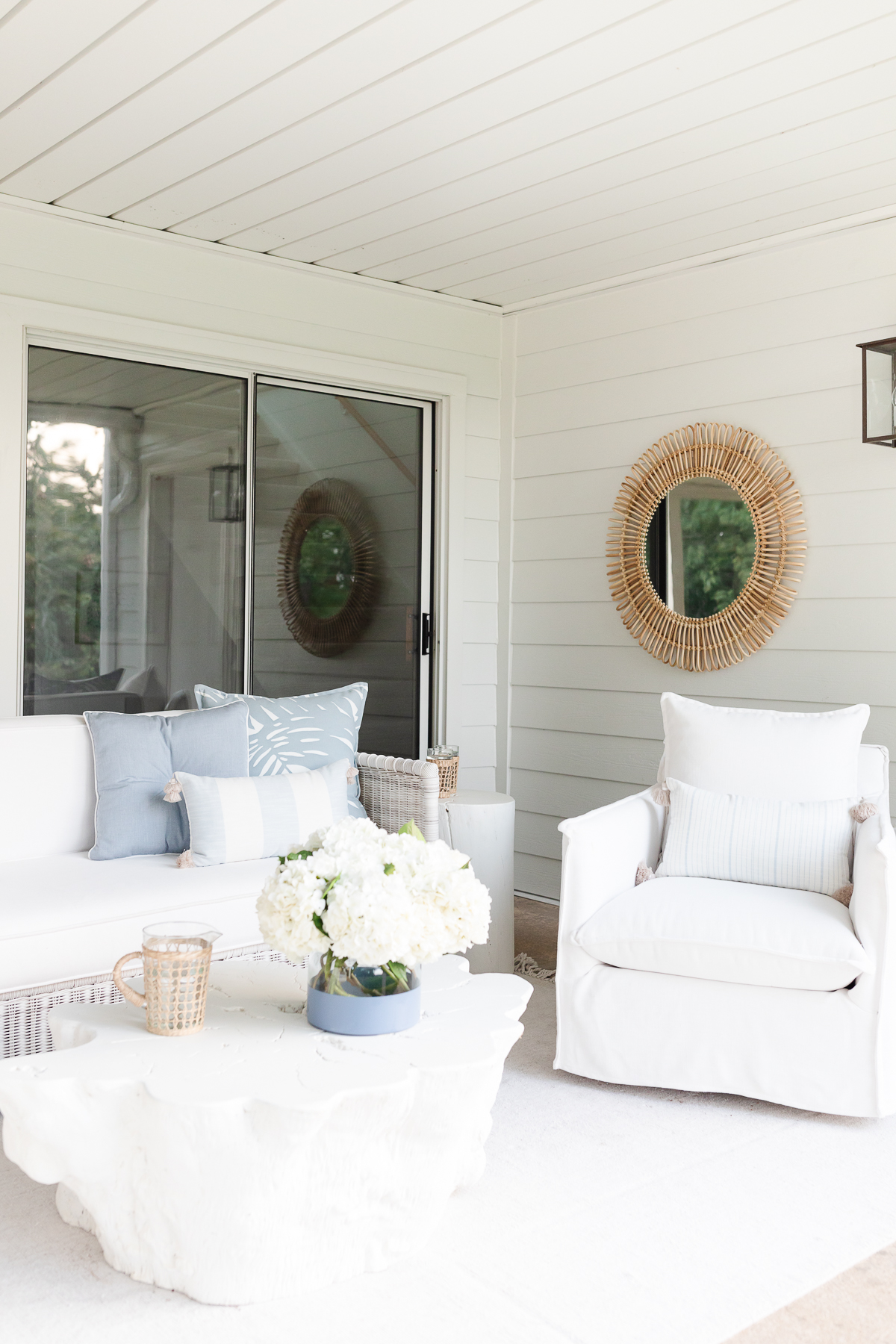 A white living room with white furniture and a white coffee table, adorned with soft outdoor pillows.