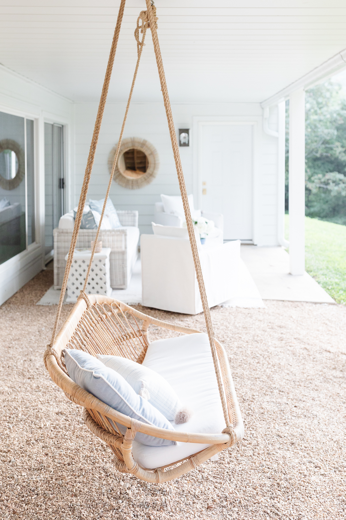 A wicker swing hanging from a porch, perfect for relaxing with outdoor pillows.