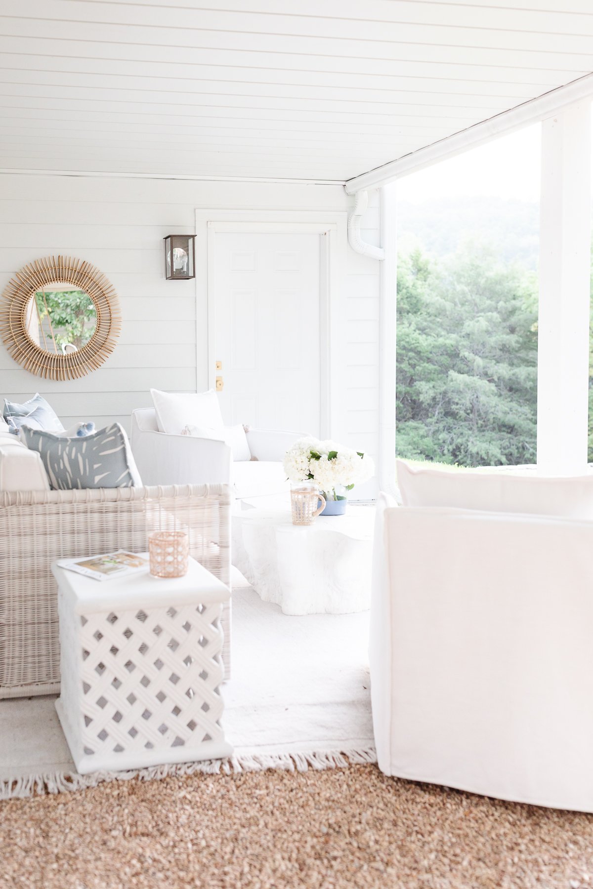 A white porch with wicker furniture and a mirror adorned with outdoor pillows.