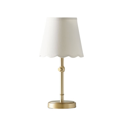 A brass table lamp with a white fabric lampshade featuring a scalloped edge offers a chic, sophisticated vibe reminiscent of the Pottery Barn Kids look for less.