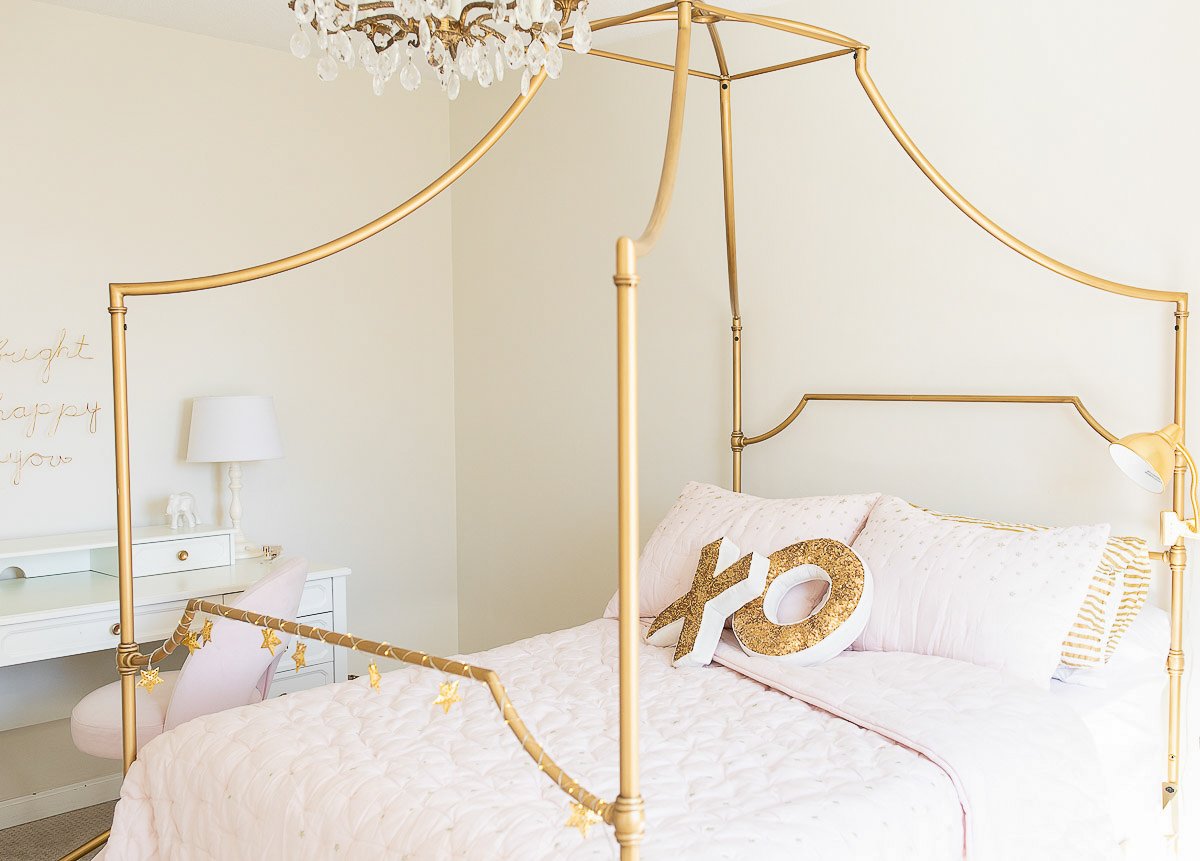 A pink and gold canopy bed in a girl's bedroom.