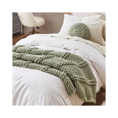 A bed with a green blanket and pillows inspired by Pottery Barn Kids.
