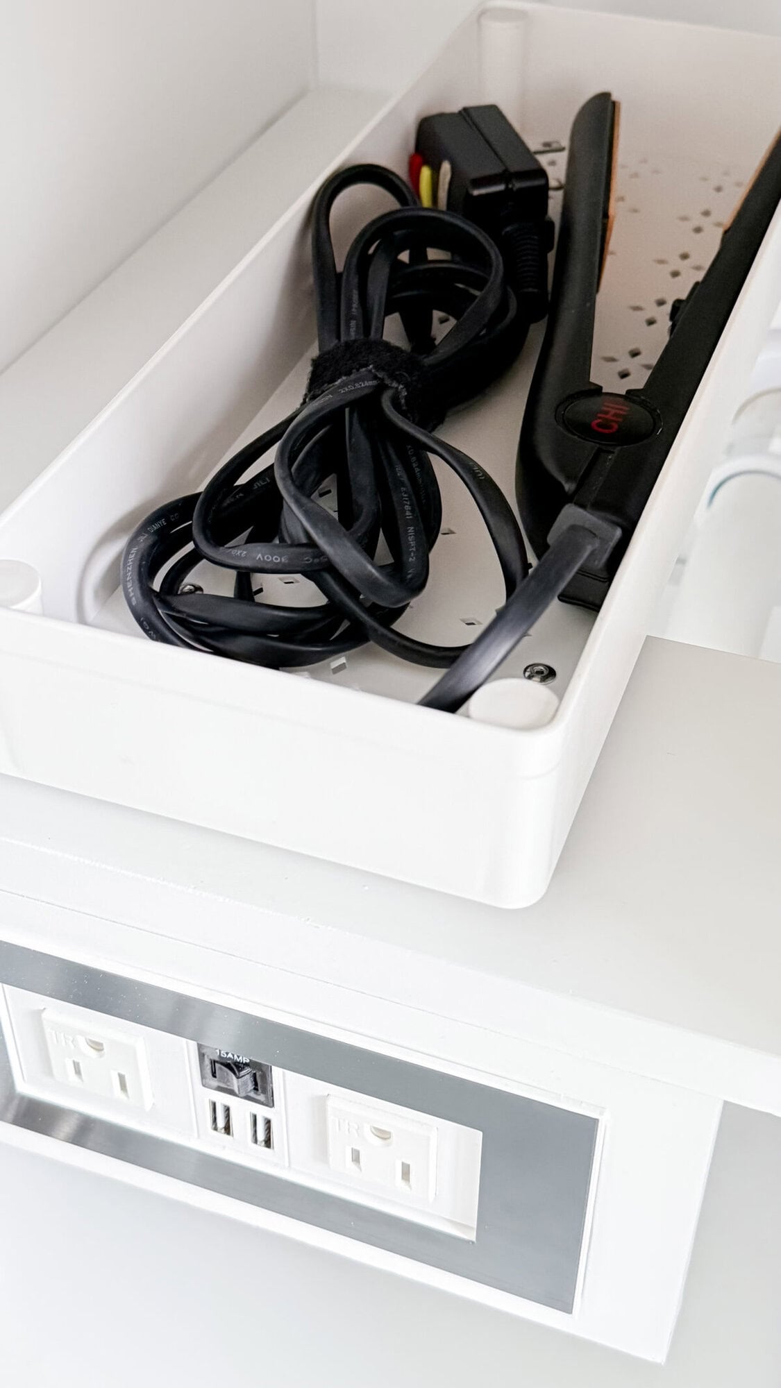 A white tray holds a hair straightener and a bundle of cables above a white outlet panel with two power sockets and two USB ports, showcasing how amazon gadgets can help organize your everyday essentials.