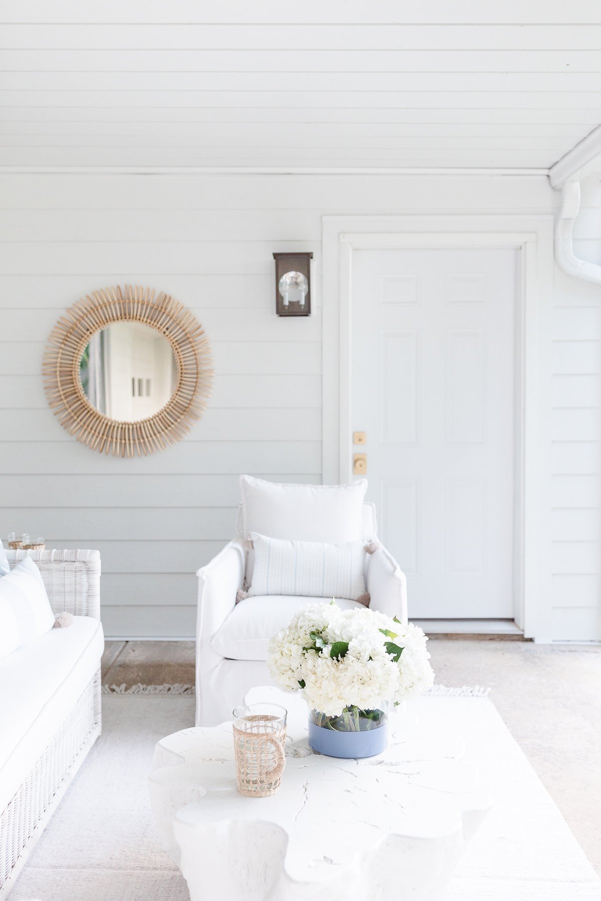 A white porch with rattan furniture and a mirror.