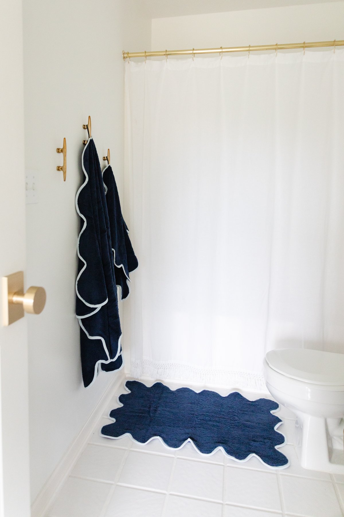 A bathroom with a white shower curtain featuring scalloped decor and a blue rug.