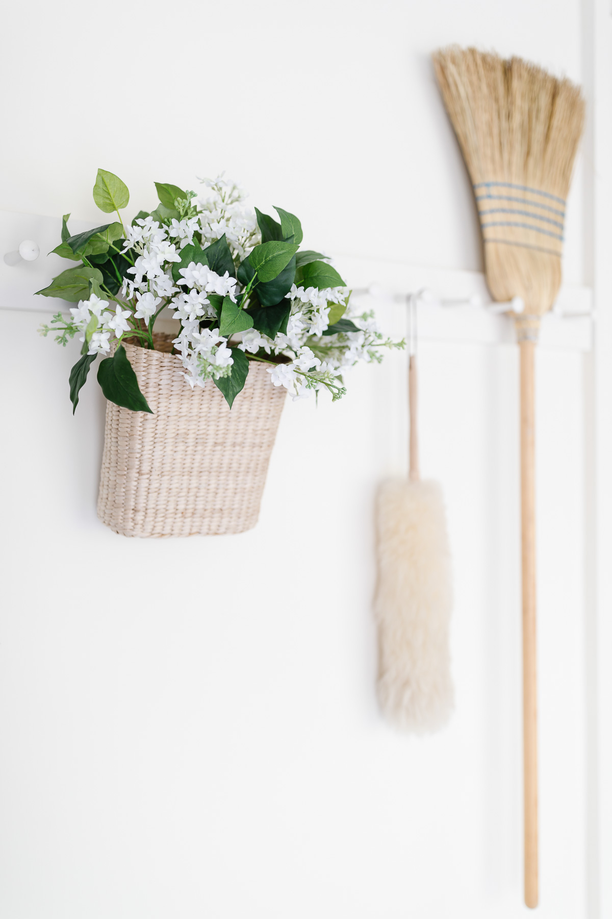 On the wall next to a basket of flowers, a broom is hanging.