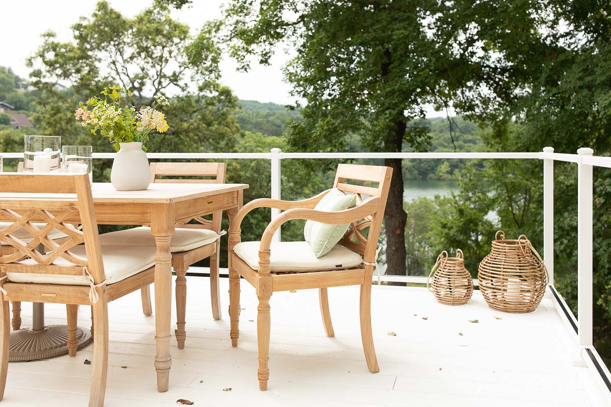 Patio furniture consisting of a wooden table and chairs on a deck overlooking a lake.