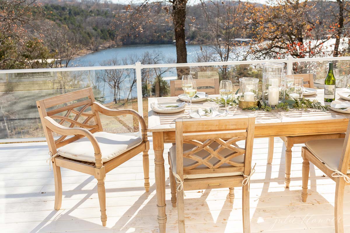Patio furniture including a wooden table and chairs on a deck overlooking a lake.