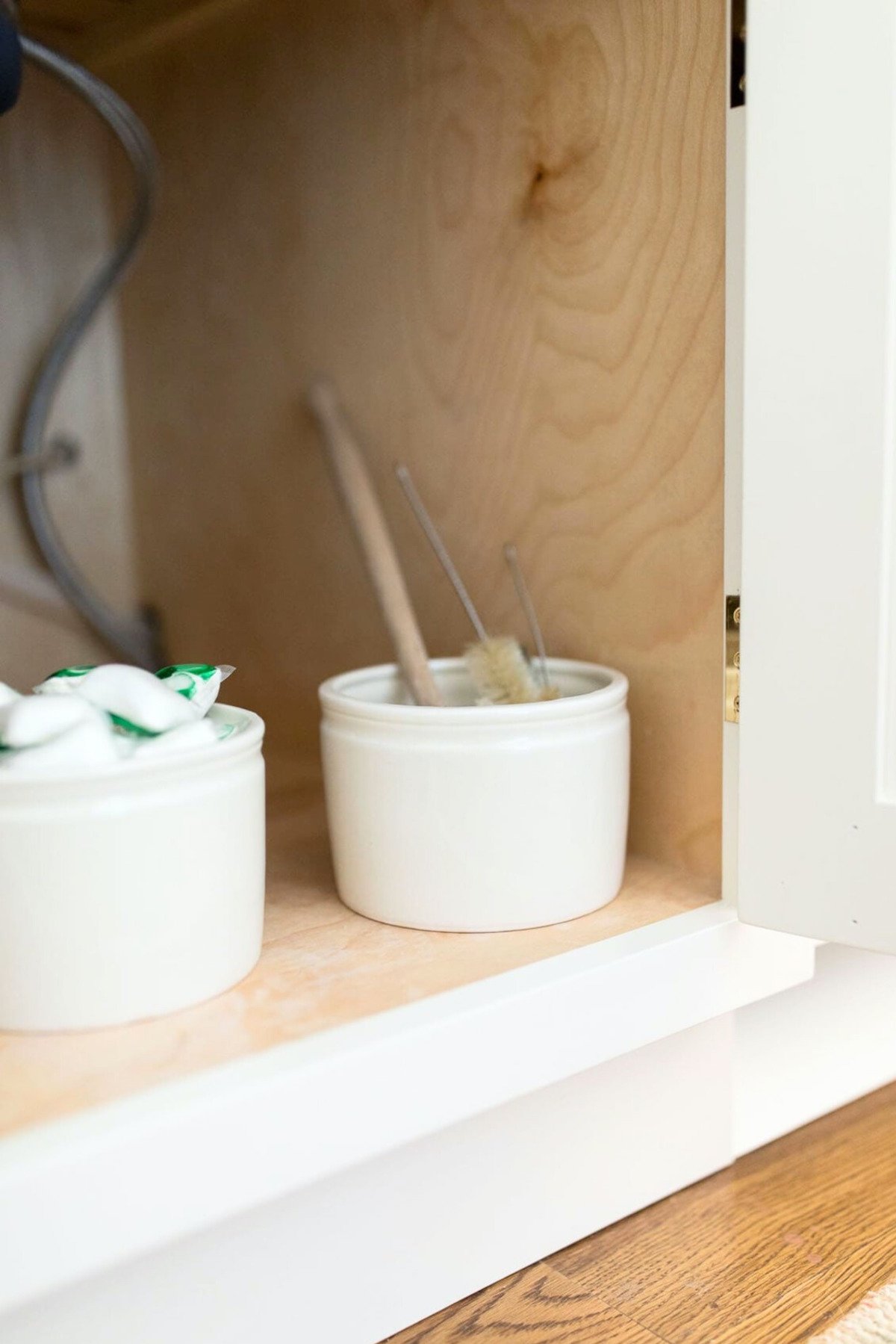 A white kitchen cabinet featuring clever under sink storage ideas for organizing two bowls of toothpaste and toothbrushes.