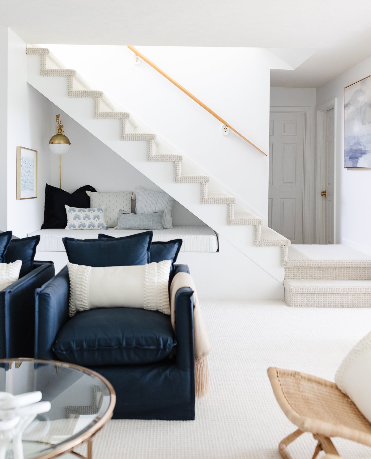 A white living room with blue furniture and a staircase.
