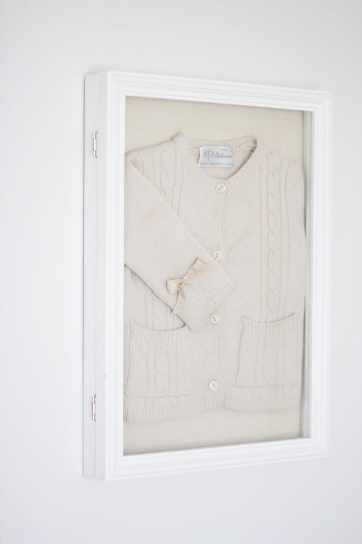 A white frame serving as stylish DIY wall decor, adorned with a white sweater.