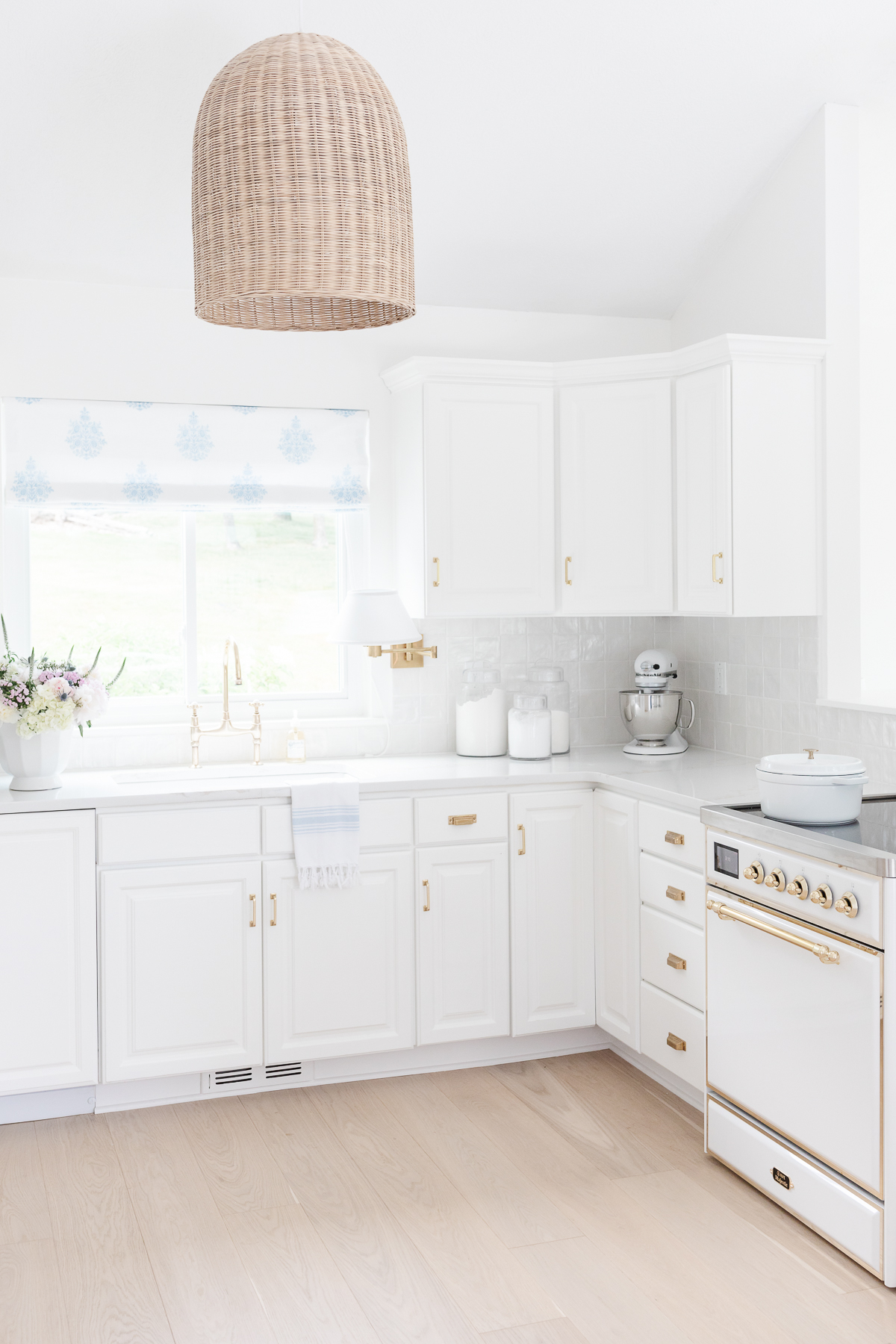 A bright, white kitchen with modern Ilve range appliances and a woven pendant lamp.