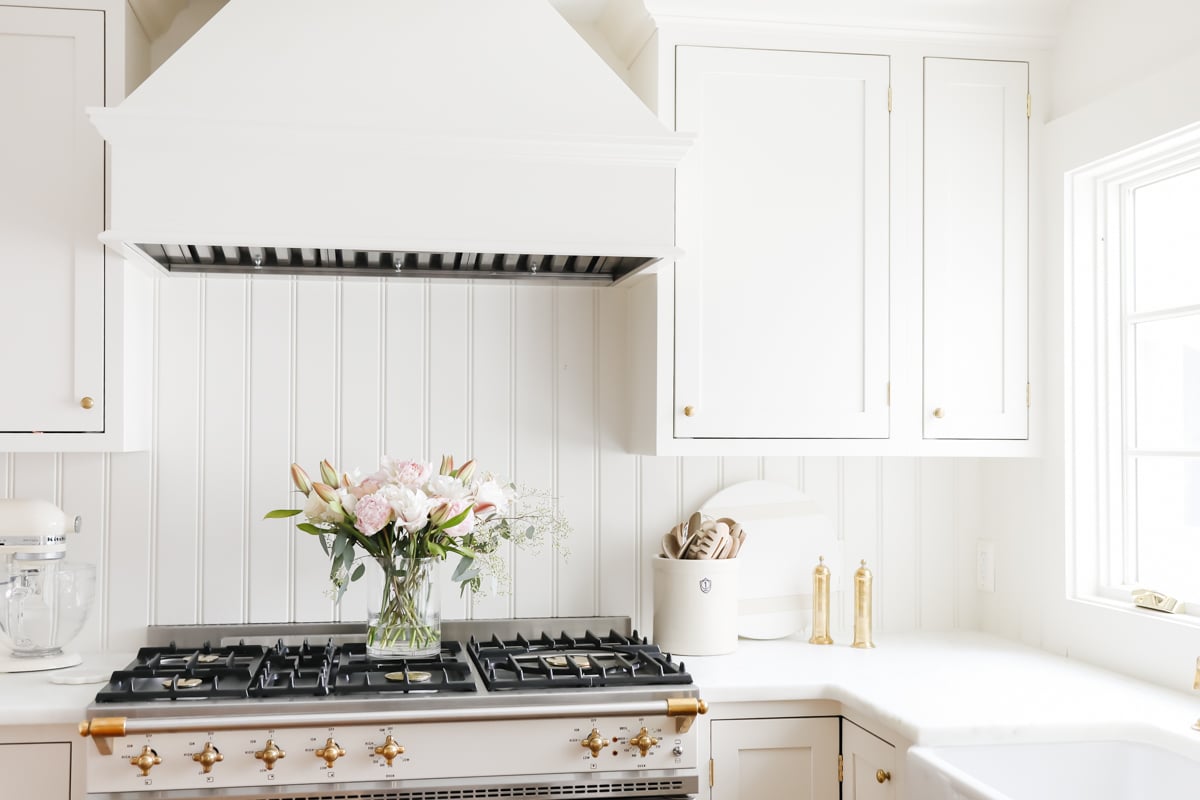 A white kitchen with a gold hood and flowers.