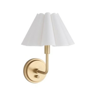 A wall-mounted sconce with a round brass base, a curved arm, and a white pleated lampshade adds timeless elegance—perfect for pairing with scalloped decor.