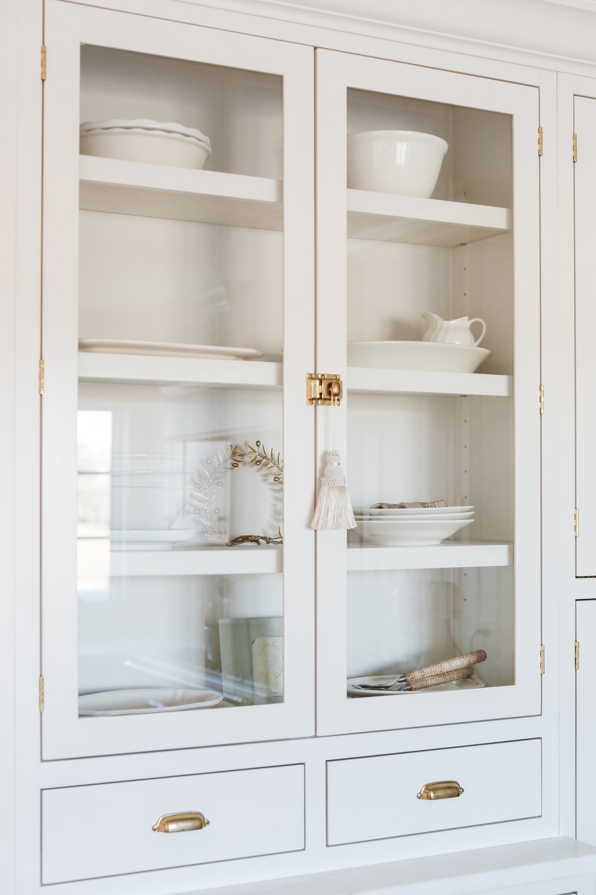 A white kitchen cabinet with glass doors displaying neatly arranged dishware and precise cabinet knob placement.