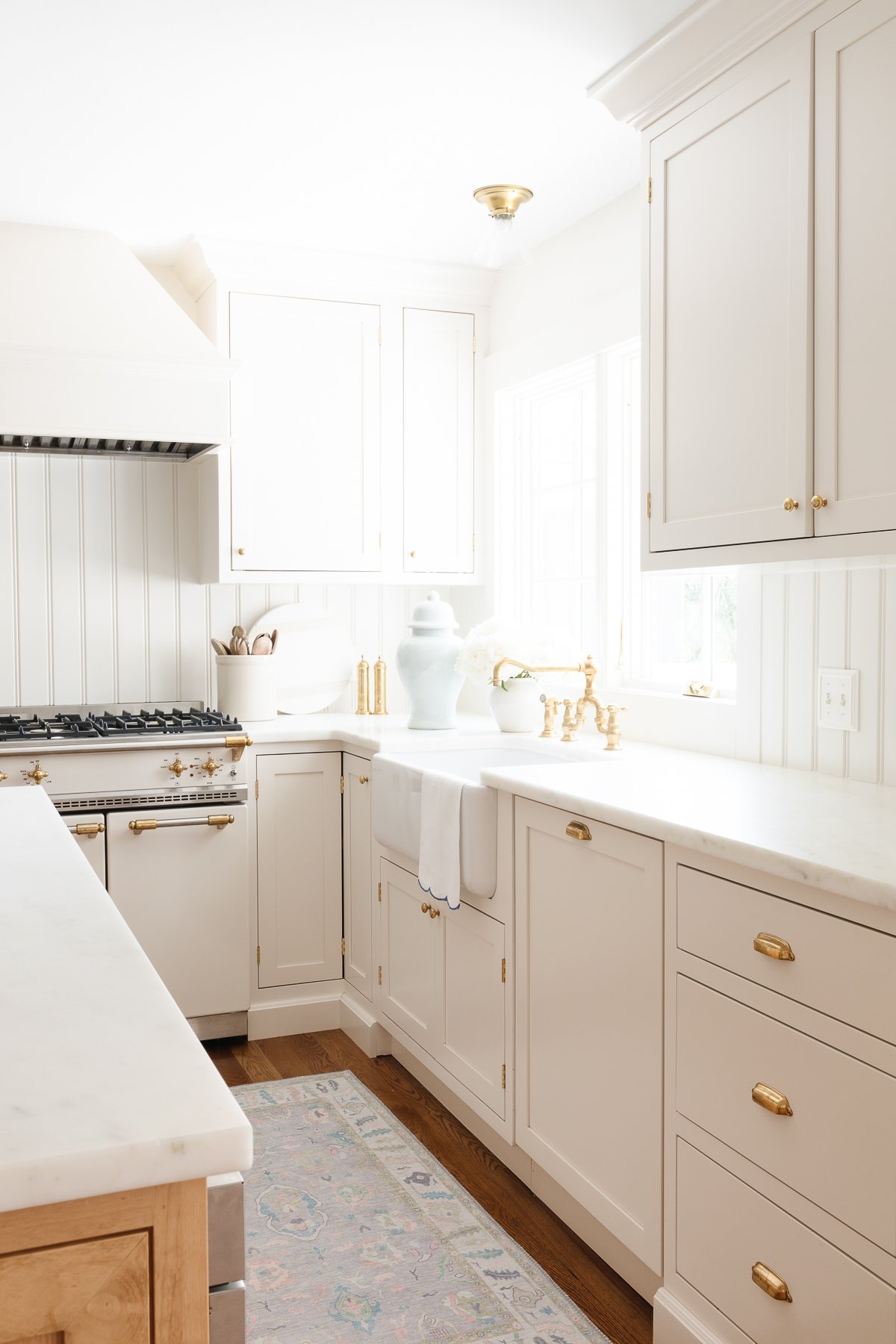 A bright, clean kitchen with white cabinetry featuring shaker cabinet knob placement, marble countertops, and brass fixtures.