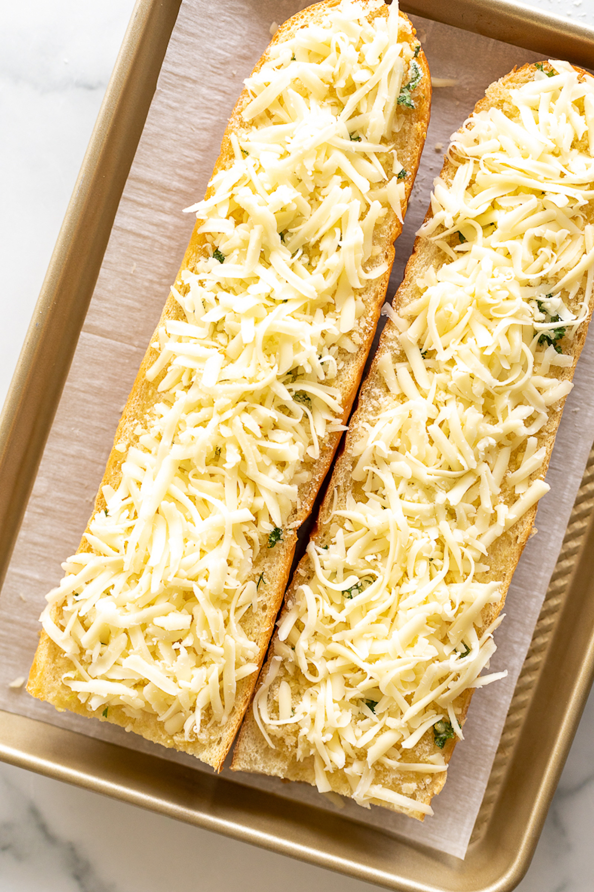 Garlic cheese bread with shredded cheese on a baking tray ready to be cooked.