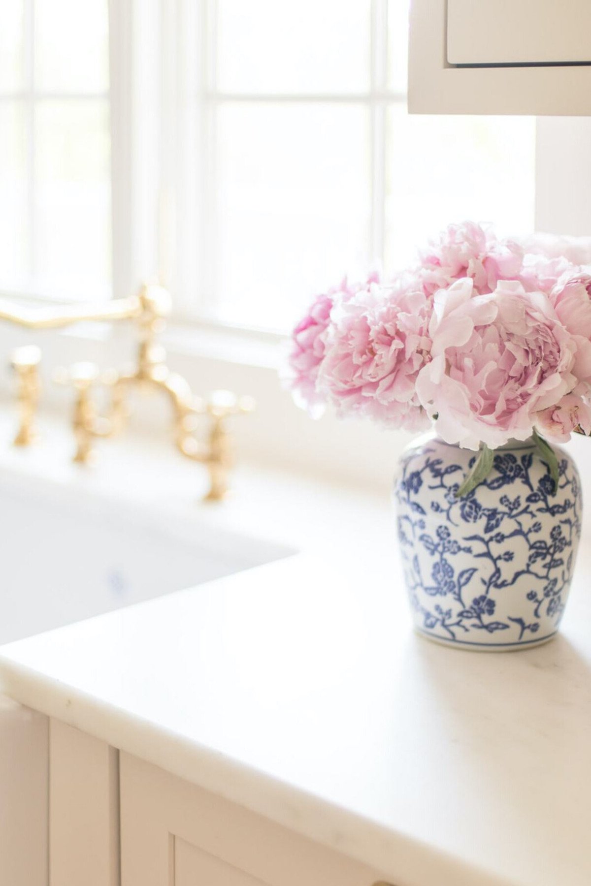 Pink and white peonies in a blue and white vase on a kitchen counter.