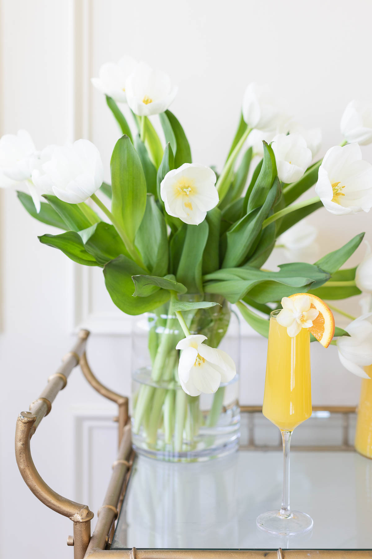 A glass of orange juice on a tray with white tulips and Easter side dishes.