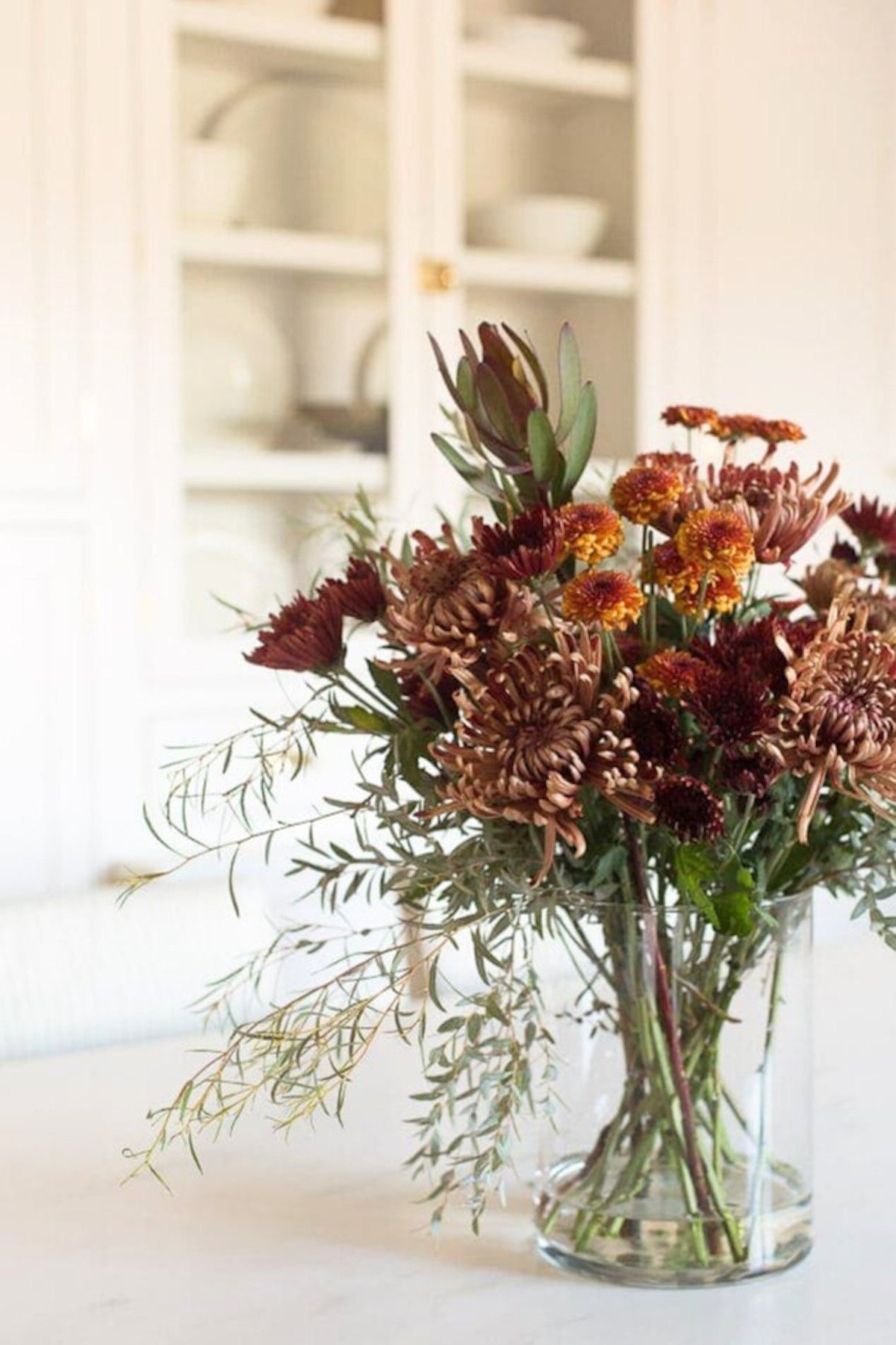 A fall centerpiece made with mums and fall foliages, on a white kitchen island. 