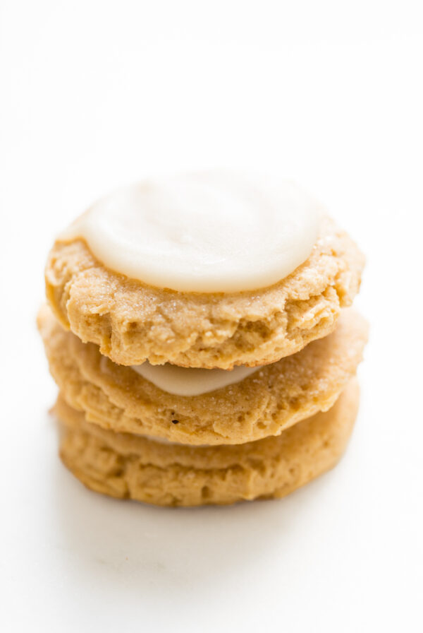 A stack of frosted pumpkin sugar cookies on a white surface