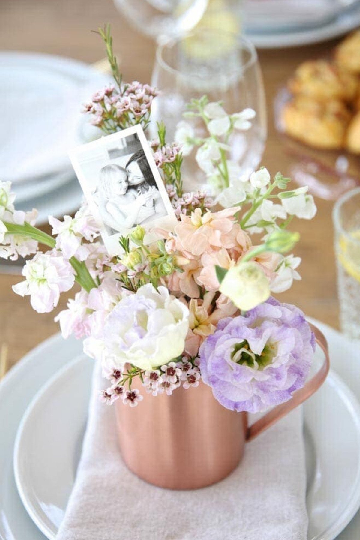 A copper mug at a mother's day place setting filled with pastel flowers and a photo of a mom and daughter