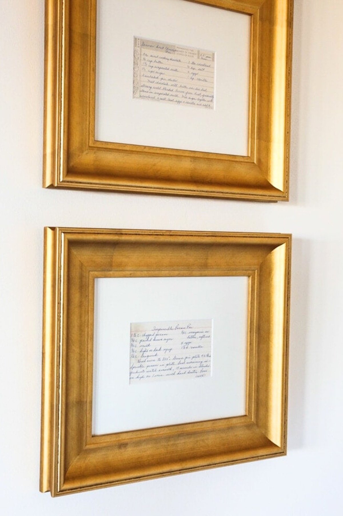 Framed recipes in wide gold frames against a white wall. 