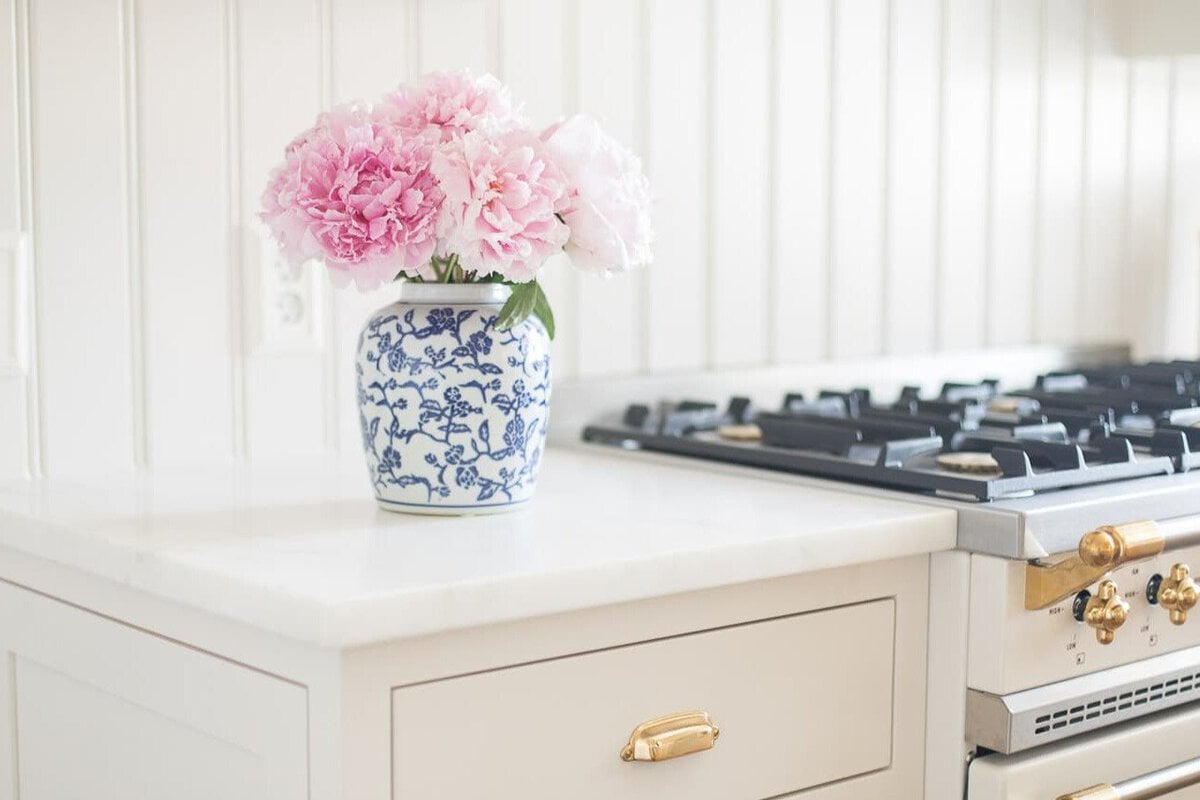 A white kitchen with pink peony flowers in a vase.