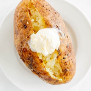 A grilled baked potato on a white plate.