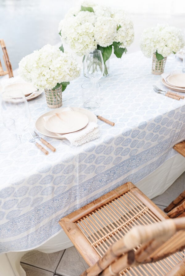 A table set with a blue block print tablecloth, with a simple flower arrangement of white hydrangeas.