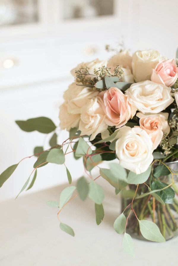 A vase of peach roses and eucalyptus in a guide for how to arrange roses