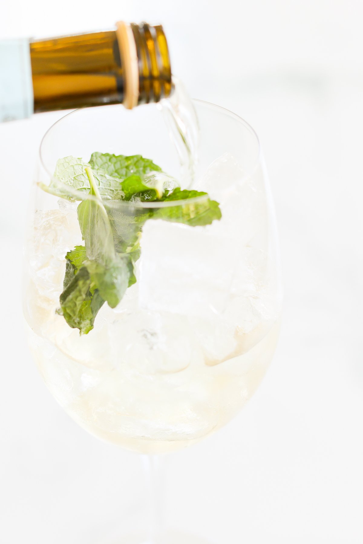 Pouring a Hugo spritz into a glass with ice and mint leaves.