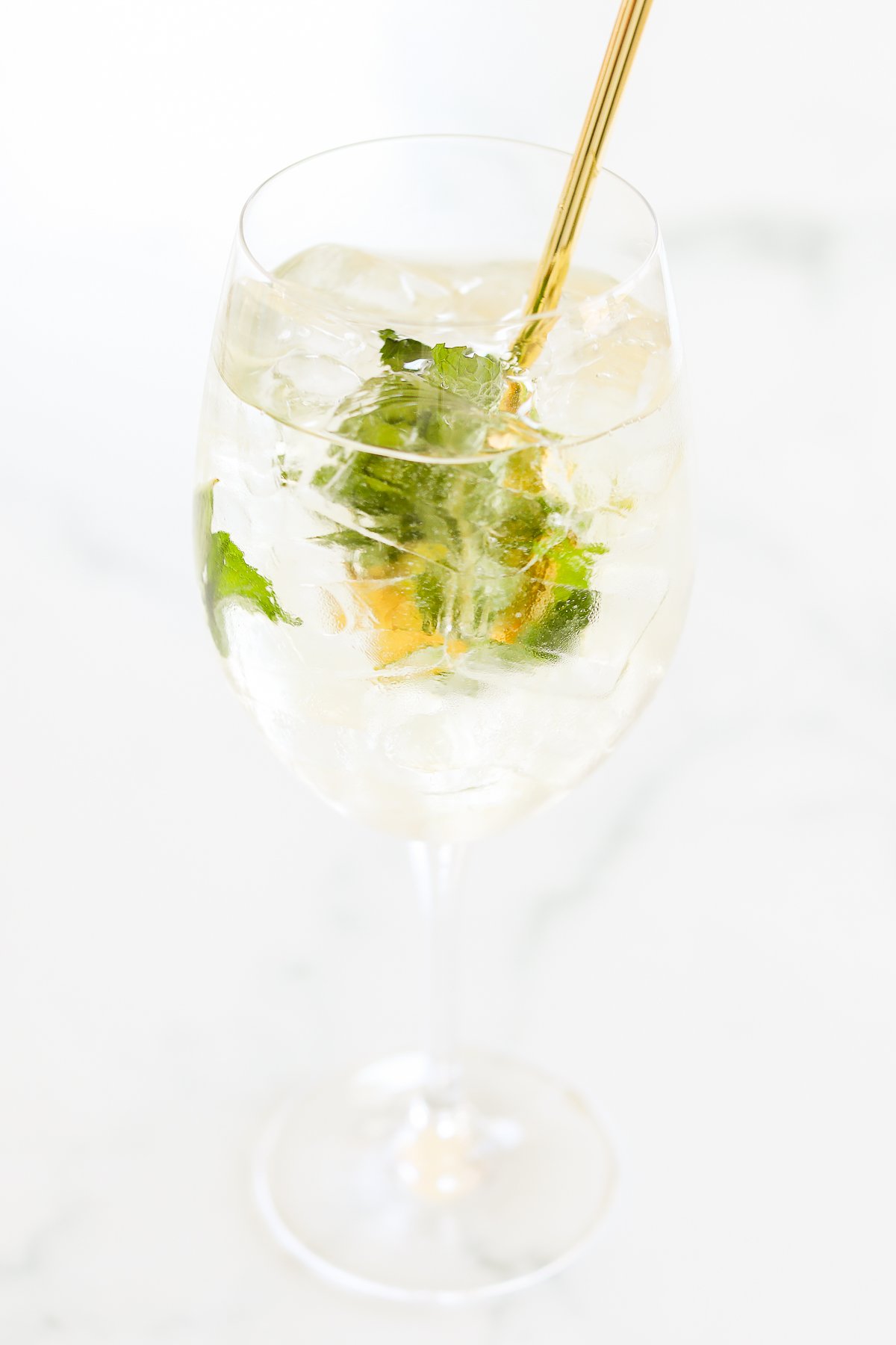 A glass of Hugo spritz garnished with fresh mint on a light background.