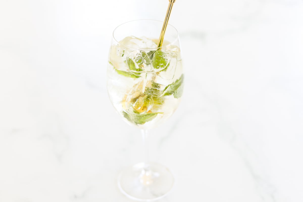 A glass of Hugo Spritz with ice and lime on a marble surface.