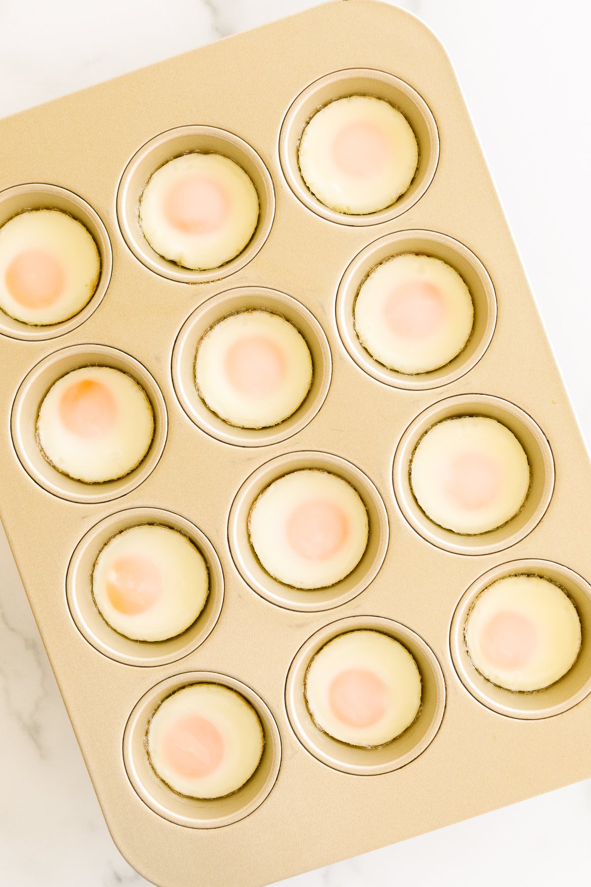 A muffin tin containing a dozen raw eggs with yolks intact.