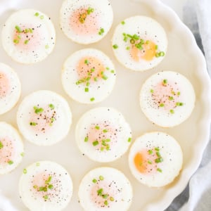 A plate of sunny side up baked muffin pan eggs garnished with herbs, pepper, and salt.