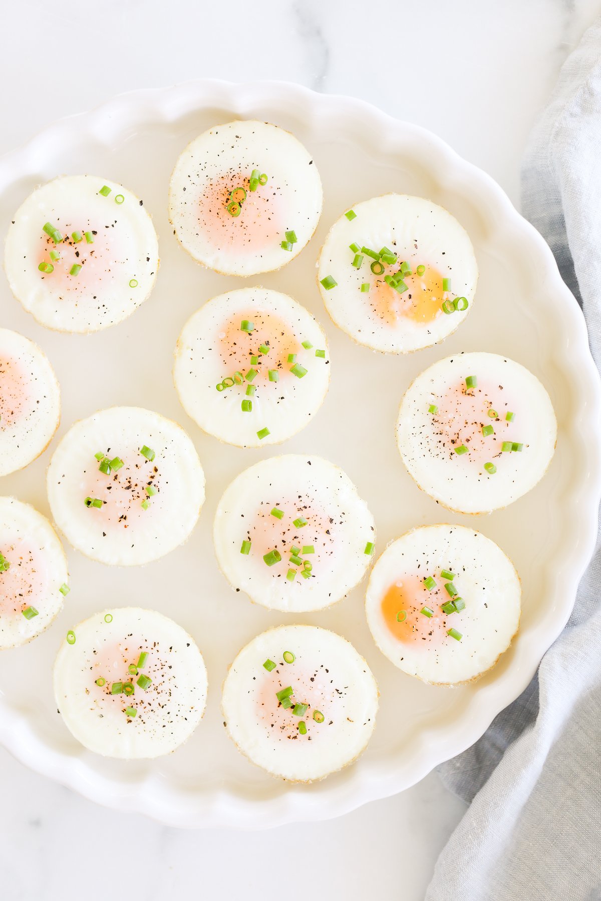 A plate of sunny side up baked muffin pan eggs garnished with herbs, pepper, and salt.
