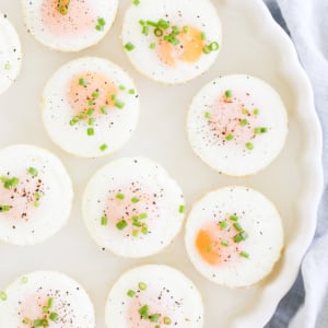 A plate of sunny side up baked muffin pan eggs garnished with herbs, pepper, and salt.