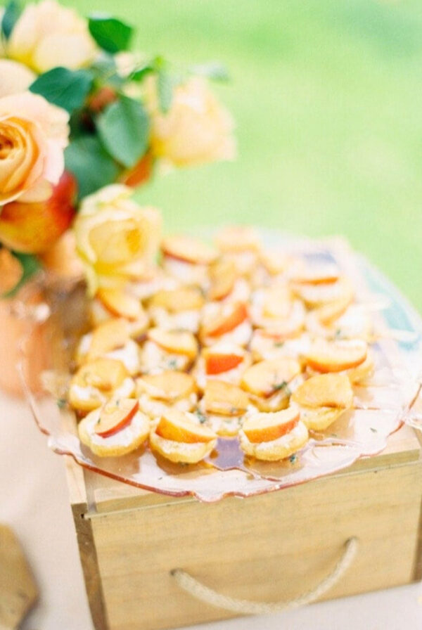peach crostini place on a plate on top of a wooden crate in an outdoor appetizer display.