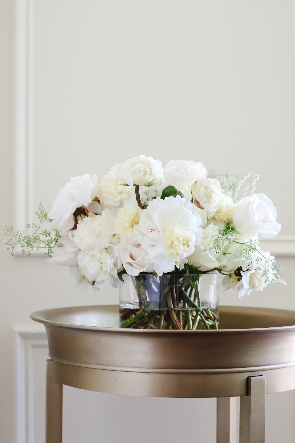 White peony flowers in a glass vase on a gold table.